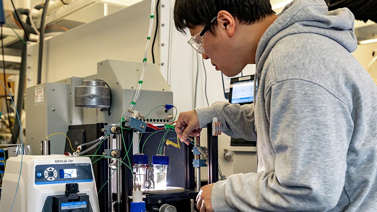 Hueynwoo Yang wearing sweatshirt and filling liquid vials with machinery at the Chase Solar Hub lab.